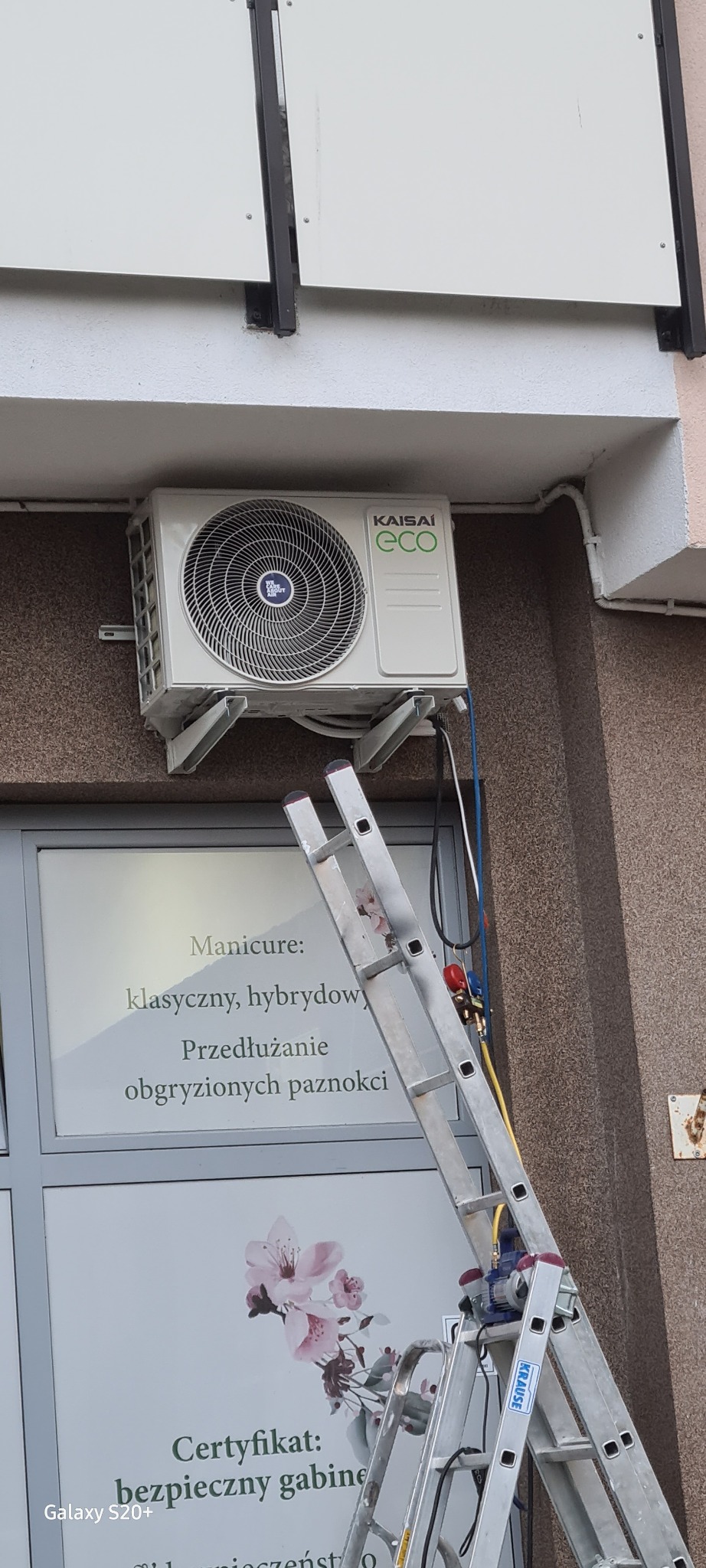 Zewnętrzna jednostka klimatyzacji Kaisai Eco zamontowana nad witryną salonu manicure, widoczna drabina i narzędzia monterskie.