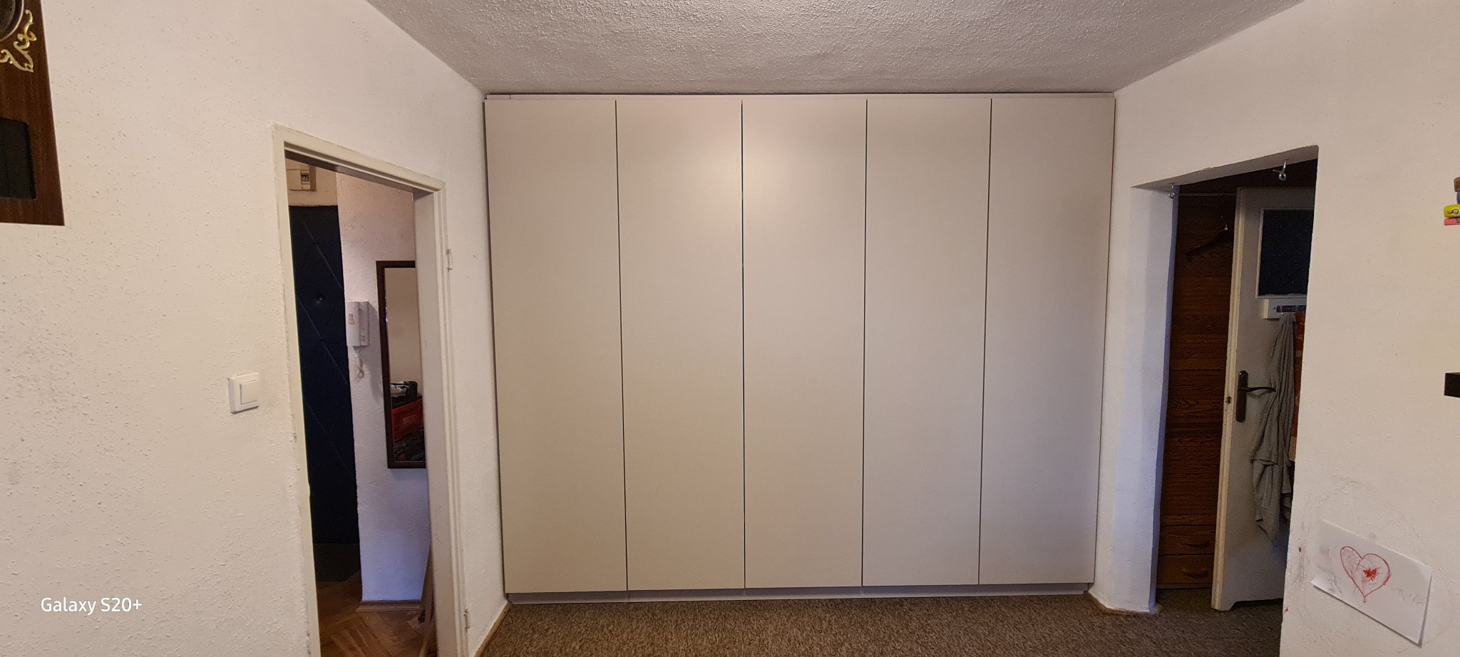 Biała szafa wnękowa z czterema drzwiami, zamontowana od podłogi do sufitu w mieszkaniu w Warszawie, widoczna z perspektywy korytarza. Po obu stronach szafy znajdują się wejścia do innych pomieszczeń.