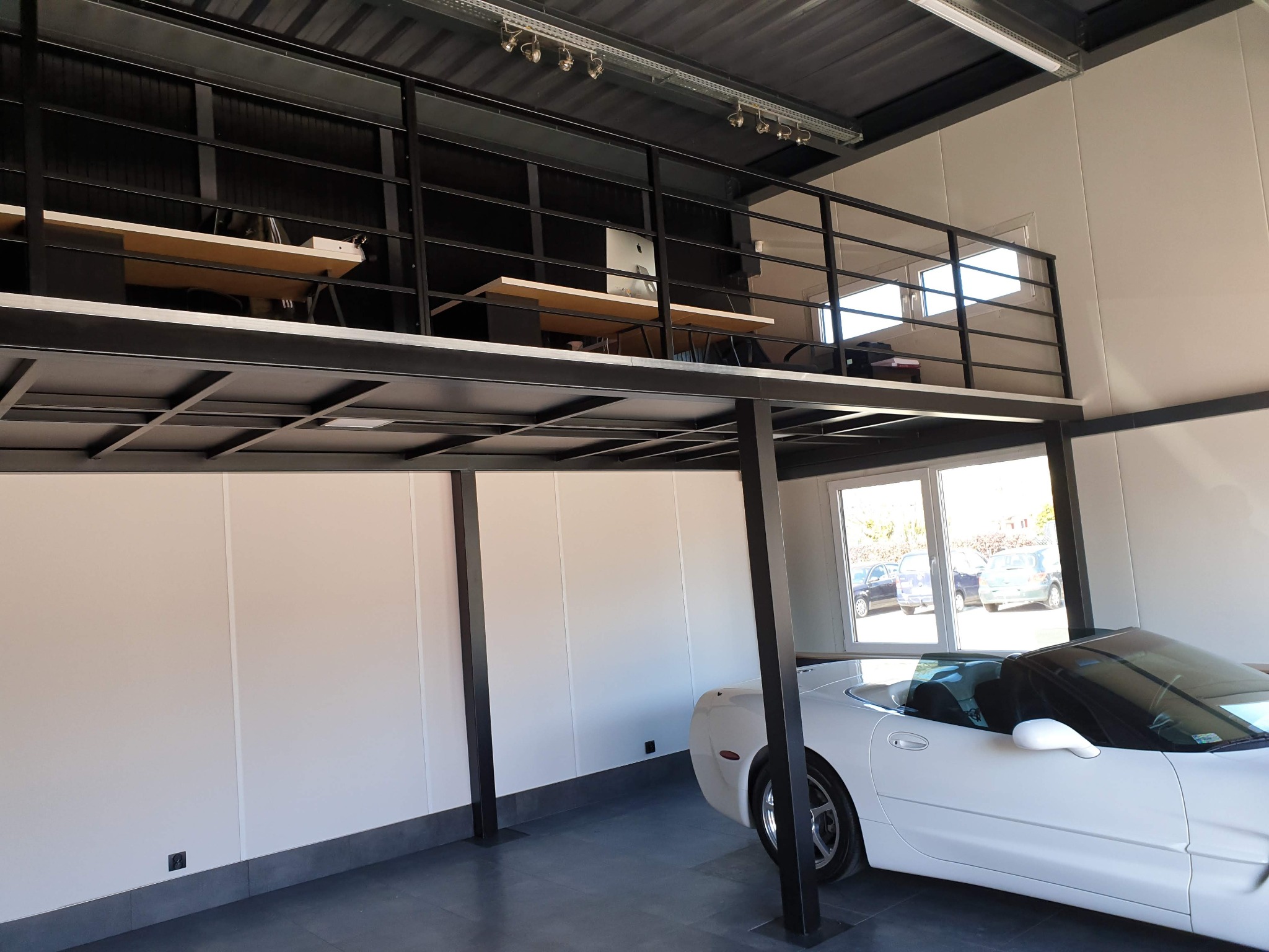 Wnętrze hali z antresolą biurową na konstrukcji stalowej, pod nią zaparkowany biały kabriolet.