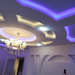 Keras Unibud - Dekoracyjny sufit podwieszany z oświetleniem LED w kolorze fioletowym i żółtym, oraz kryształowy żyrandol w wykończonym wnętrzu.
