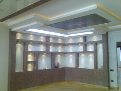 Wykończona ściana z wnękami oświetlonymi punktowymi lampami, dekoracyjny sufit podwieszany z oświetleniem LED, brązowo-beżowa kolorystyka.