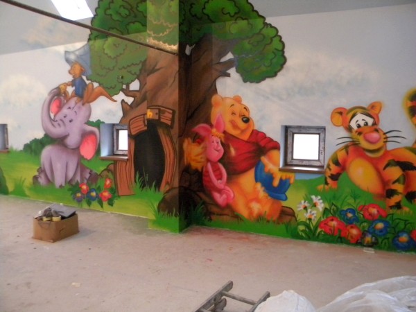 Malowidło ścienne przedstawiające postacie z Kubusia Puchatka: Prosiaczka, Puchatka, Tygryska i słonia z kapeluszem, wykonane w pokoju dziecięcym; widoczne okna i karton na podłodze.