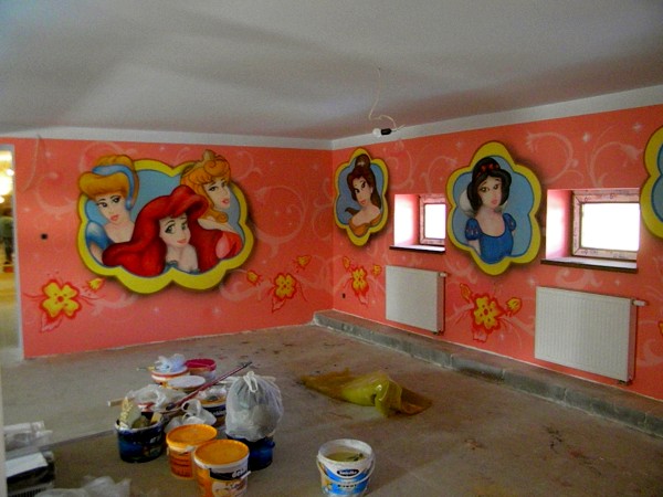 Pokój z pomalowanymi ścianami przedstawiającymi postacie z bajek Disneya, widoczne pędzle i farby, stanowiące zaplecze artystyczne w trakcie pracy.