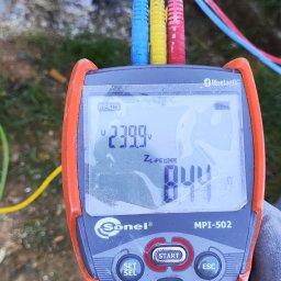 Atom Elektryka - Miernik Sonel MPI-502 z kolorowymi przewodami, wskazujący napięcie 239.9V i rezystancję 844 omów, trzymany w rękawicy ochronnej.