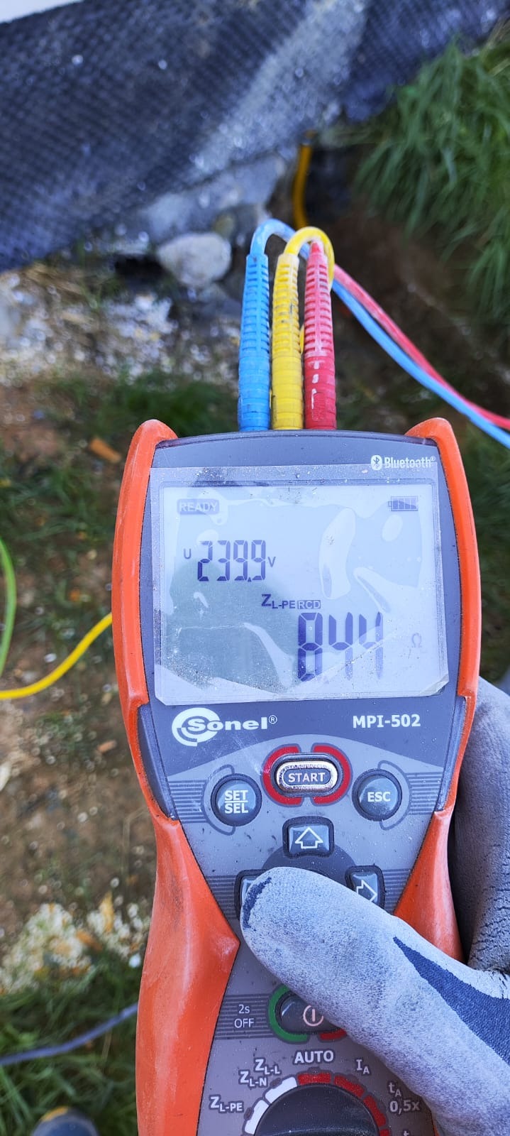 Miernik Sonel MPI-502 z kolorowymi przewodami, wskazujący napięcie 239.9V i rezystancję 844 omów, trzymany w rękawicy ochronnej.