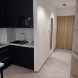 ŁUKASZ STAWSKI - Nowoczesna kuchnia z czarnymi szafkami i marmurowym backsplashiem, widok na przedpokój z drewnianymi drzwiami i oświetleniem punktowym.