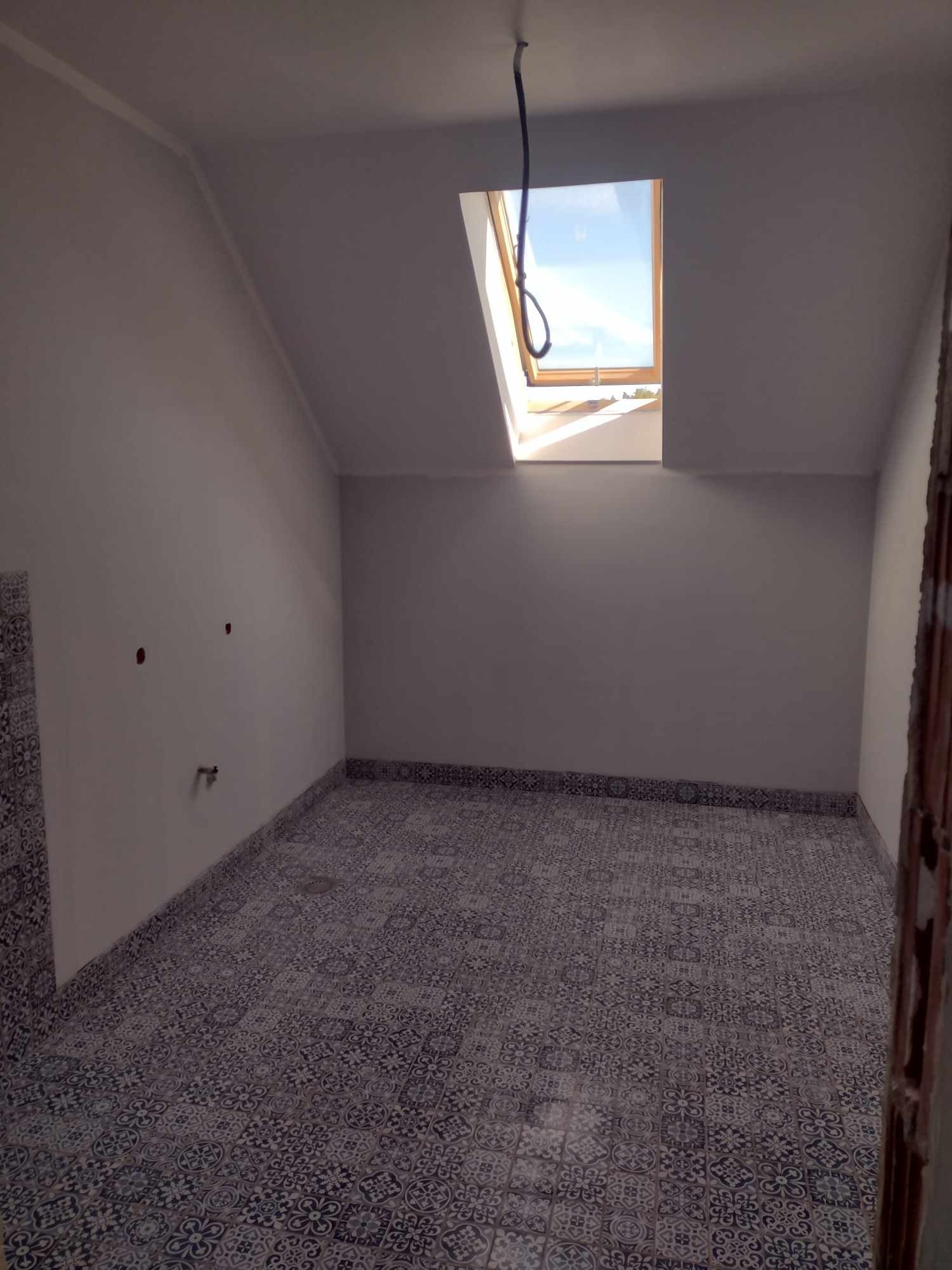 Poddasze po remoncie z nową, wzorzystą podłogą z płytek ceramicznych, widoczne okno dachowe i przewody elektryczne.