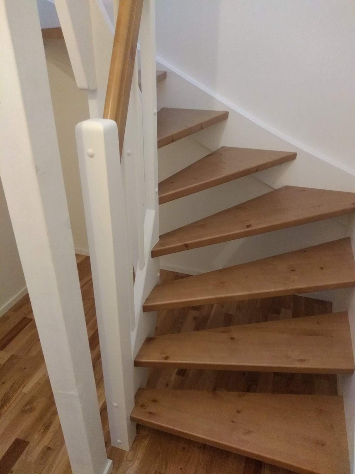 Drewniane schody z białymi balustradami i lakierowanymi stopniami, widoczne z dołu, z fragmentem parkietu na podłodze