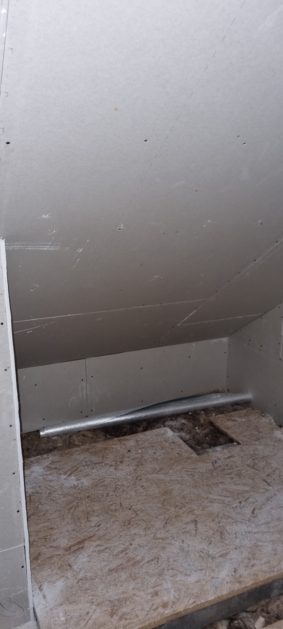 Niedokończone poddasze: zamontowana płyta gipsowo-kartonowa, widoczny przewód wentylacyjny i surowa podłoga z płyty OSB.