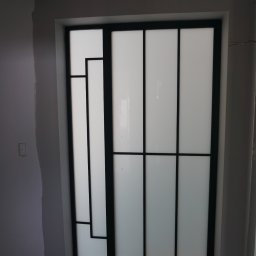 PROFIL - Nowoczesne drzwi przesuwne z czarną ramą i mlecznym szkłem w trakcie montażu, widoczne zabezpieczenia podłogi.