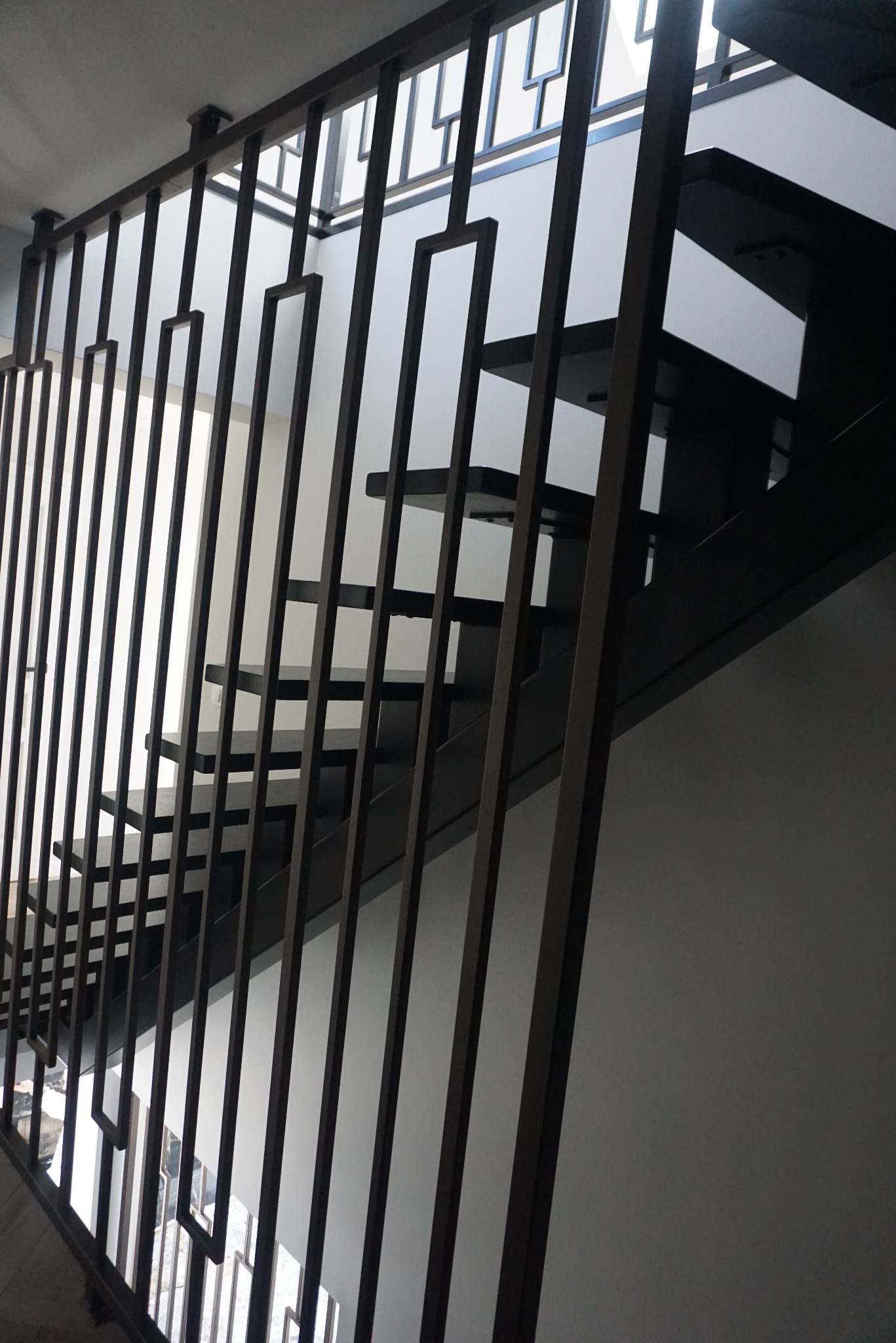Nowoczesne schody z ciemnymi stopniami i metalową balustradą o geometrycznym wzorze, widziane pod kątem od dołu.
