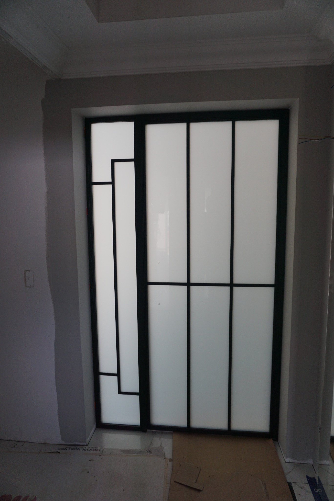 Nowoczesne drzwi przesuwne z czarną ramą i mlecznym szkłem w trakcie montażu, widoczne zabezpieczenia podłogi.