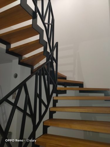 Spiralne schody z drewnianymi stopniami i czarną, geometryczną balustradą z metalu.