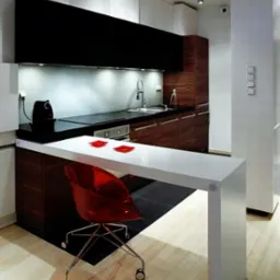 Nowoczesna kuchnia z białymi i drewnianymi szafkami, czarnym blatem, oświetleniem punktowym i czerwonym krzesłem barowym.