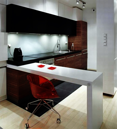 Nowoczesna kuchnia z białymi i drewnianymi szafkami, czarnym blatem, oświetleniem punktowym i czerwonym krzesłem barowym.