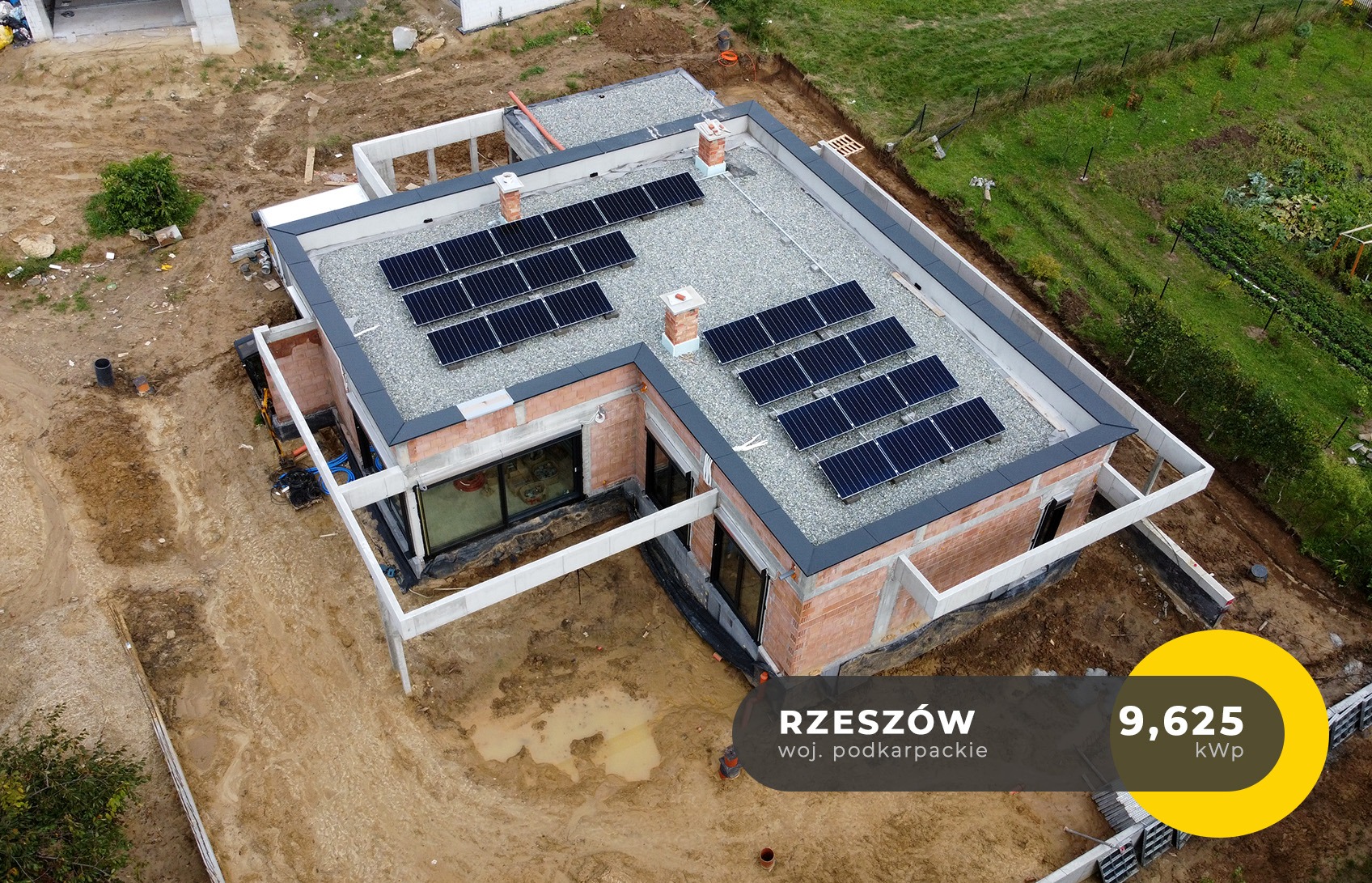 Widok z drona na dom jednorodzinny w trakcie budowy z zainstalowanymi panelami słonecznymi na płaskim dachu pokrytym żwirem, Rzeszów.