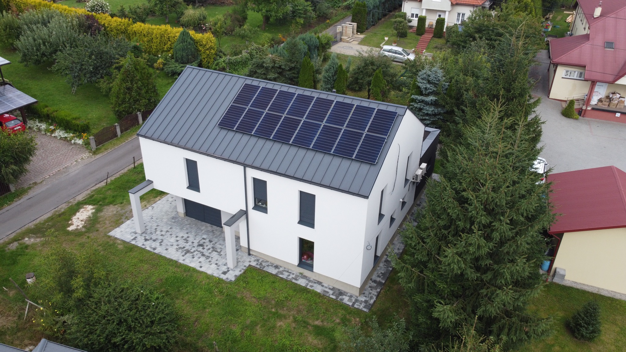 Nowoczesny dom jednorodzinny z szarym dachem i panelami słonecznymi na dachu, widok z lotu ptaka.