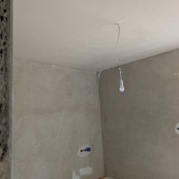 Cezary krawczyk - Ściany i sufit po szpachlowaniu, gotowe do malowania. Widoczne gniazdka elektryczne i prowizoryczne oświetlenie żarówką. Tekstura ścian z efektem dekoracyjnym.