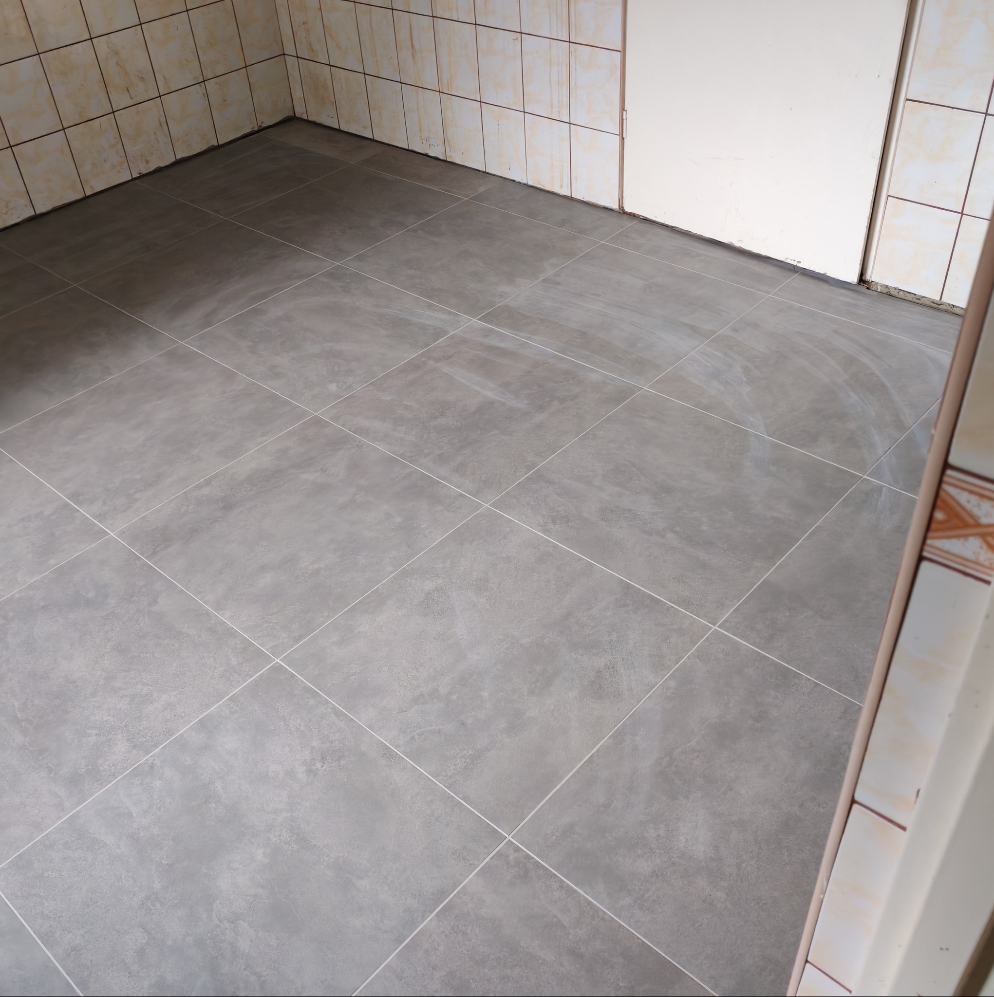 Szare płytki podłogowe w łazience z beżowymi płytkami ściennymi i białymi drzwiami. Widok z góry, ukończona realizacja.