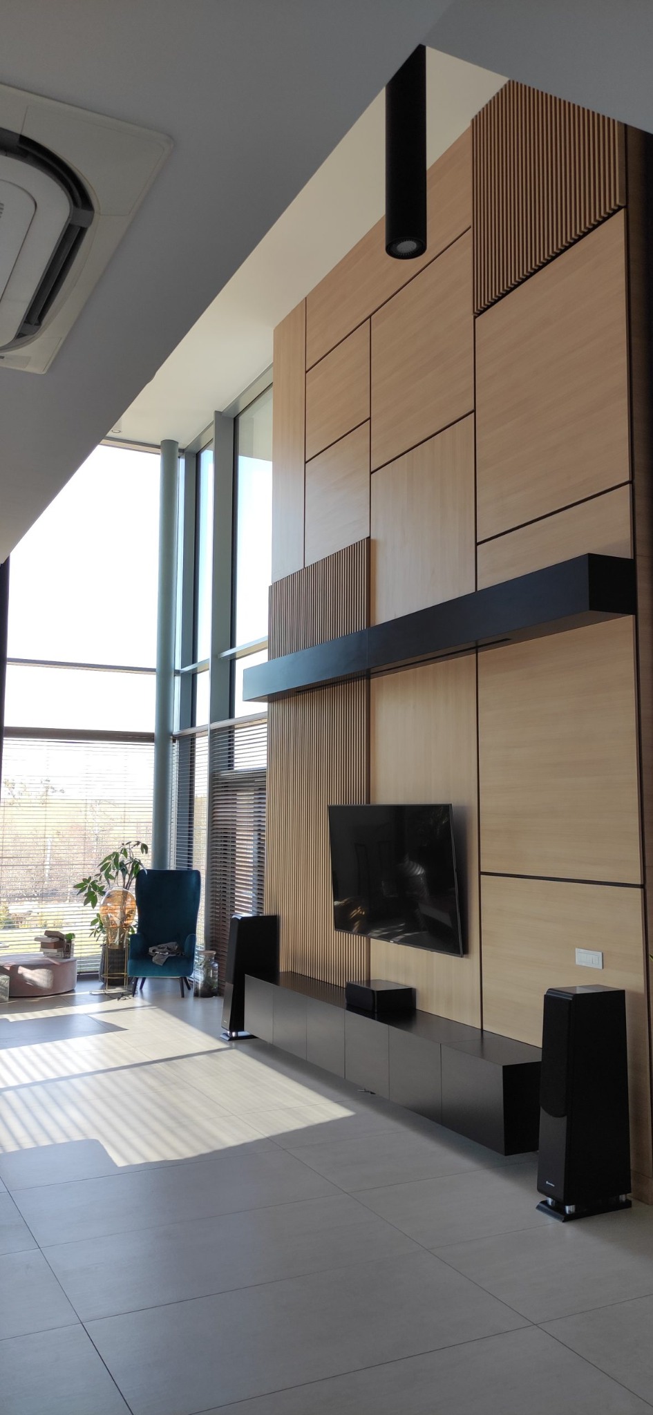 Nowoczesna ściana telewizyjna z jasnego drewna i czarnymi akcentami, obejmująca szafkę RTV i półkę wiszącą, w jasnym salonie z dużym oknem.