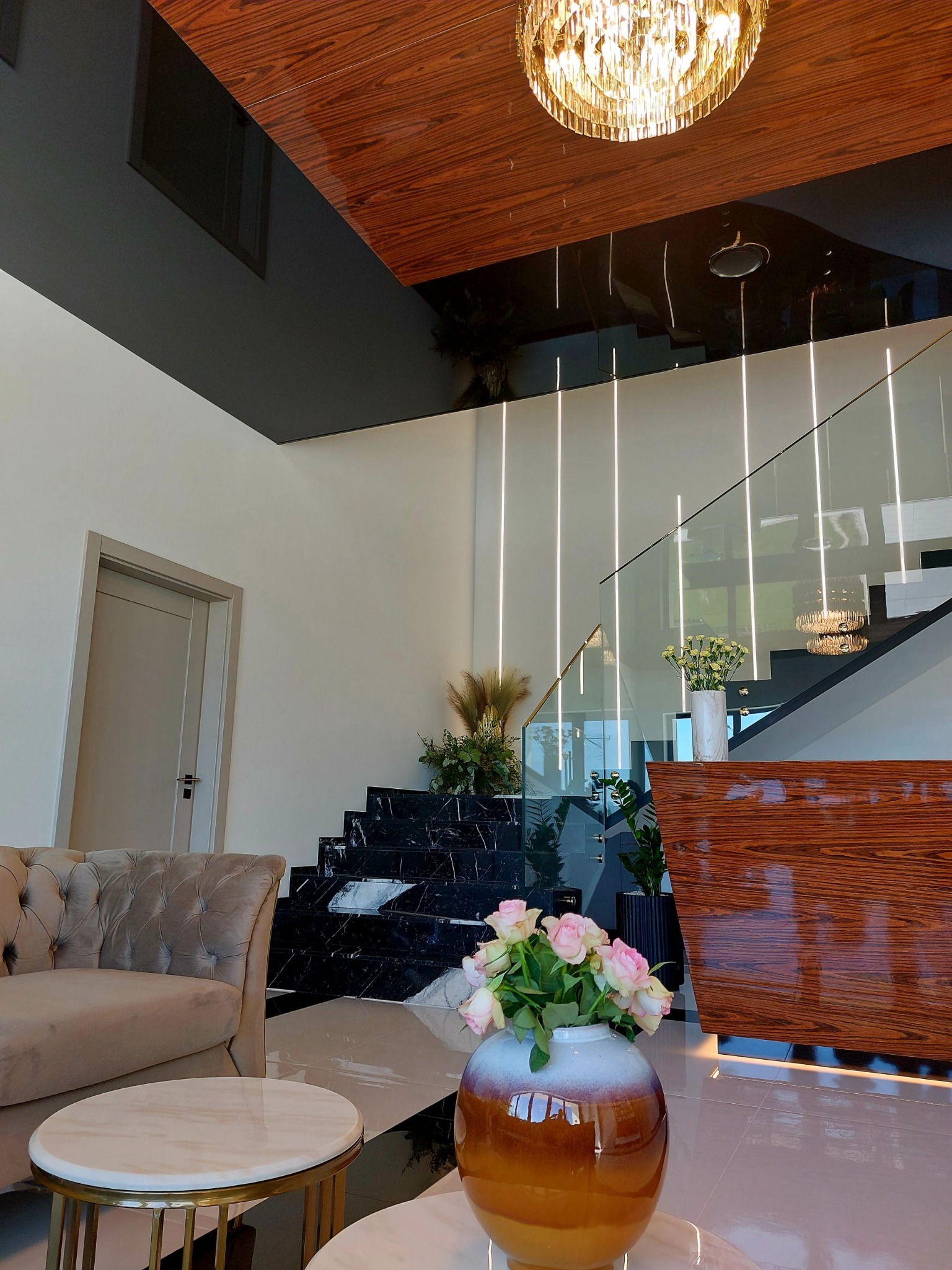 Nowoczesne wnętrze z marmurowymi schodami, szklaną balustradą, drewnianym sufitem i designerskim oświetleniem.