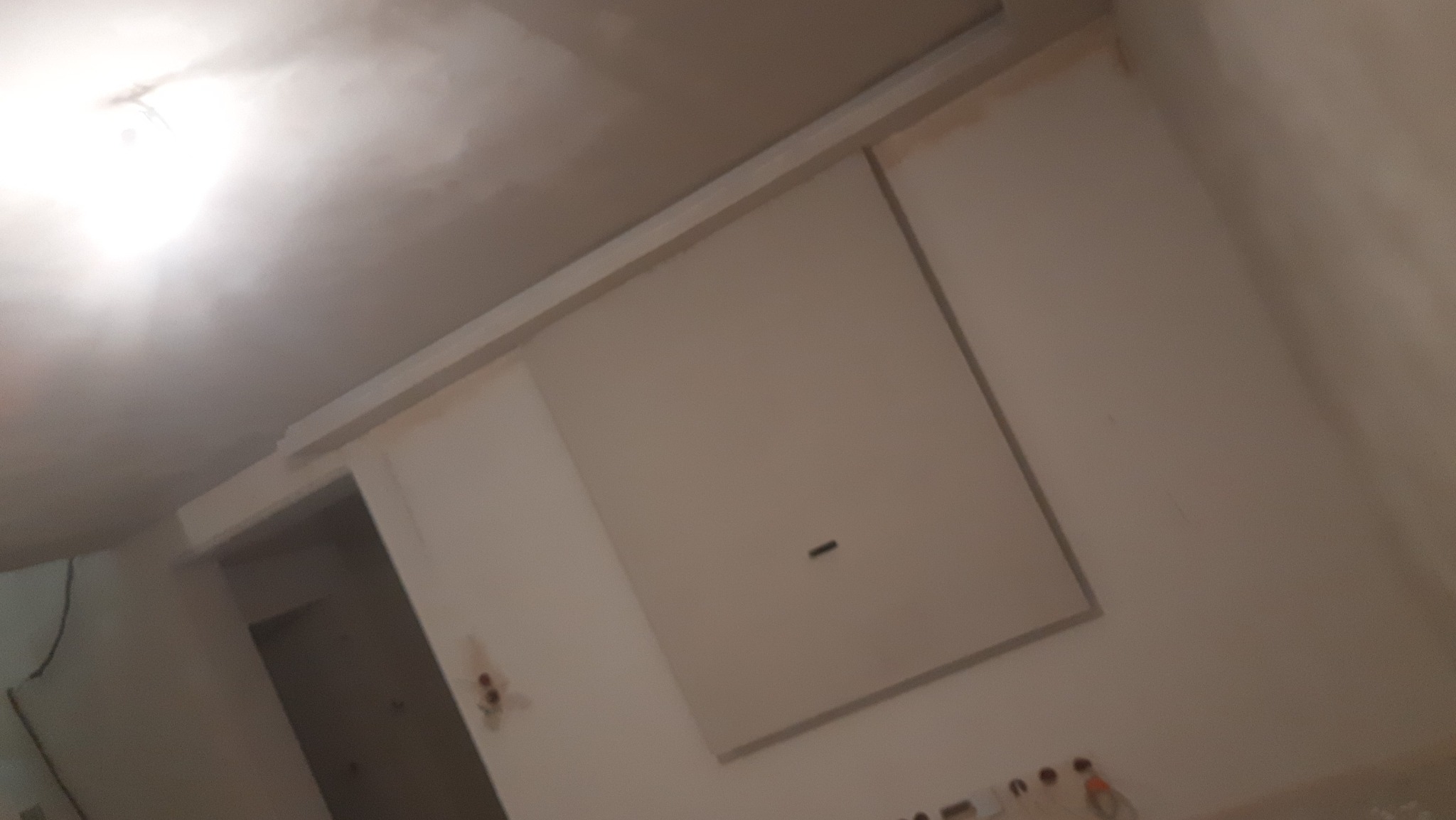 Ściana i sufit po szpachlowaniu, widoczne ślady po gładzi, przygotowane do malowania, z zamontowaną listwą maskującą.