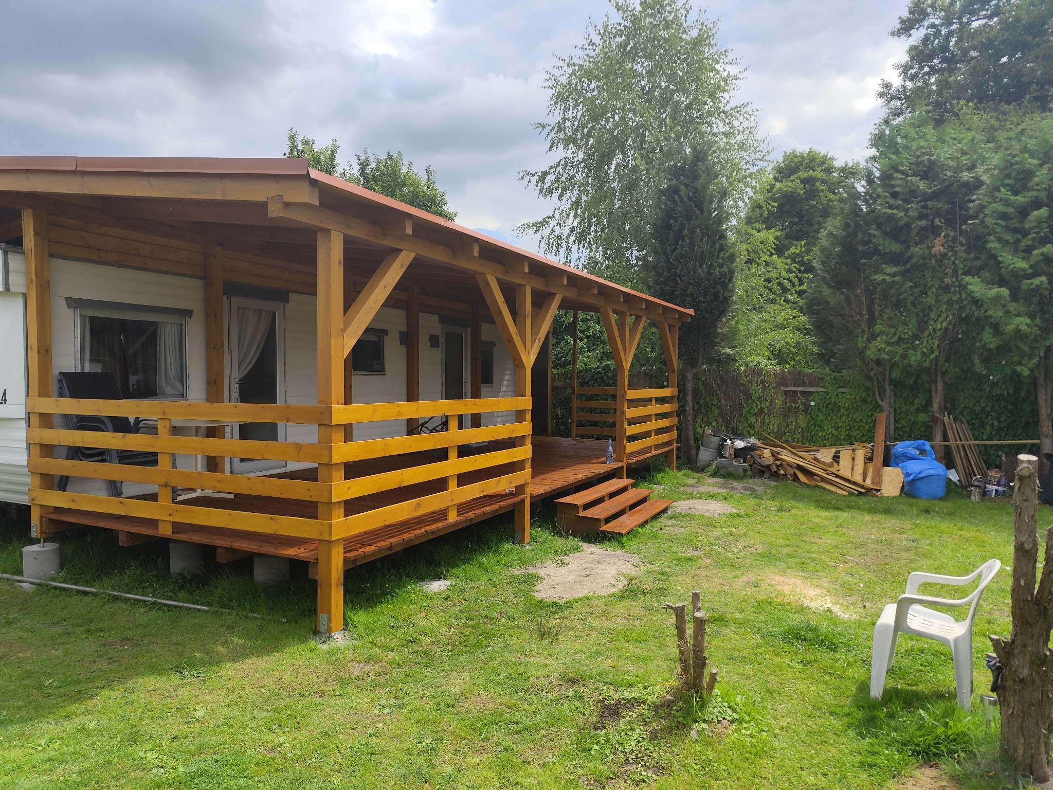 Domek letniskowy z drewnianą konstrukcją dachu i werandą, widoczne elementy więźby dachowej, świeżo pomalowane drewno i zielone otoczenie.