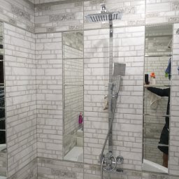 LuxBud Vladyslav Sirobaba - Wykończona łazienka z białymi płytkami imitującymi cegłę, dekoracyjnymi pasami i lustrami wkomponowanymi w ścianę. Widoczna armatura prysznicowa.