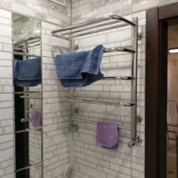 Biała łazienka z eleganckimi płytkami, grzejnikiem drabinkowym z ręcznikami i lustrem, tworząca sp&oacute;jną aranżację wnętrza.