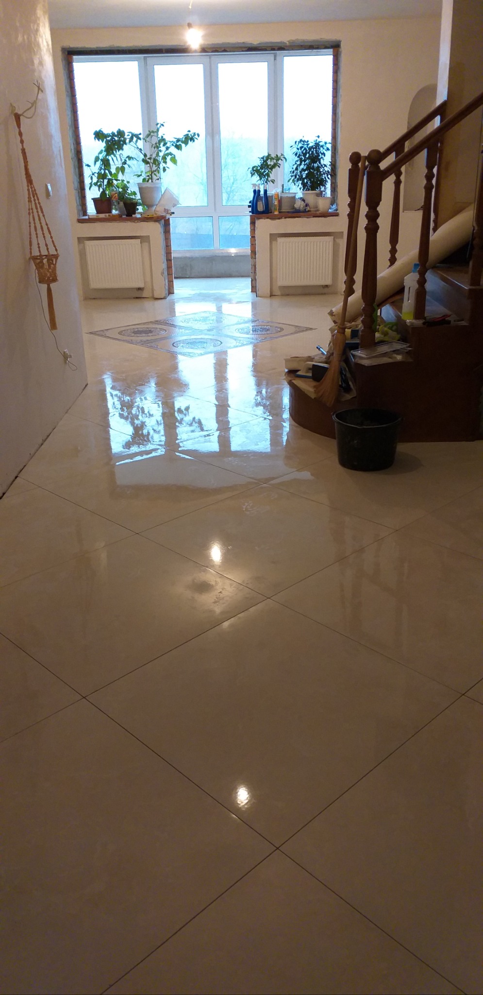 Połyskująca, kremowa podłoga z płytek ułożonych w karo, z dekoracyjnym wzorem przy oknie. Widoczne schody, wiadro i akcesoria. Świeże wykończenie wnętrza.