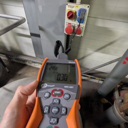Wojciech Zaczek - Pomiary elektryczne w Gliwicach: Miernik Sonel MPI-507 w trakcie pracy, wskazujący wartości na tle gniazd przemysłowych i instalacji elektrycznej.