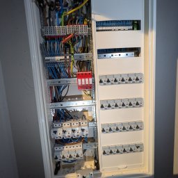 Wojciech Zaczek - Rozdzielnica elektryczna z licznymi przewodami i zabezpieczeniami, widok z bliska, ukazujący skomplikowaną strukturę i precyzję wykonania instalacji.