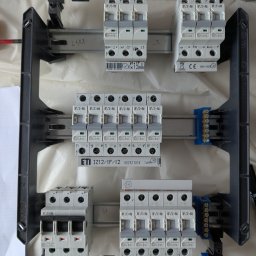 Wojciech Zaczek - Rozdzielnica elektryczna z zamontowanymi bezpiecznikami Eaton i listwami zaciskowymi, widok z góry. Elementy zamocowane na szynie DIN w czarnej obudowie.