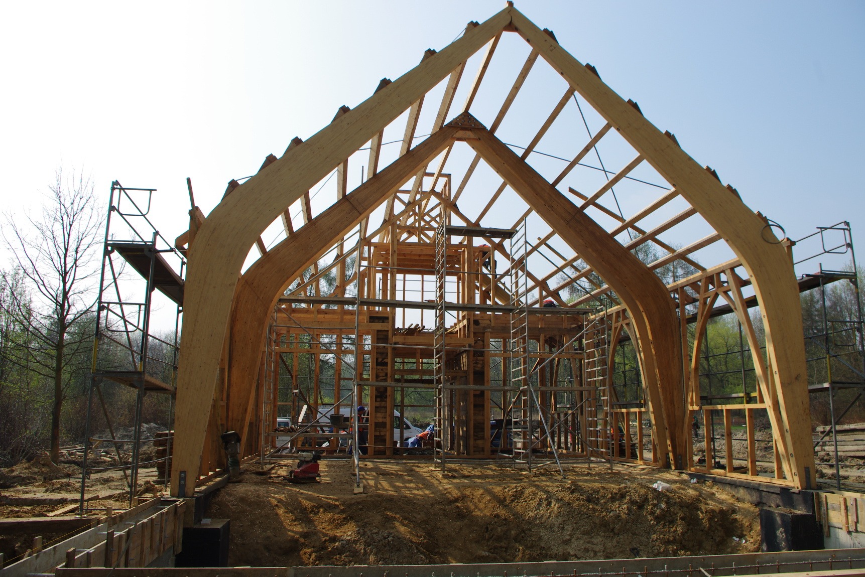 Konstrukcja szkieletowa domu z charakterystycznymi łukowymi elementami nośnymi z drewna klejonego, widoczne rusztowania i fundamenty w trakcie budowy, Chorzów.