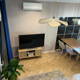 BartHome Bartłomiej Chrapek - Nowoczesne wnętrze salonu z klimatyzatorem ściennym, drewnianą podłogą w jodełkę i lampą w kształcie kwiatu. Widok z góry.