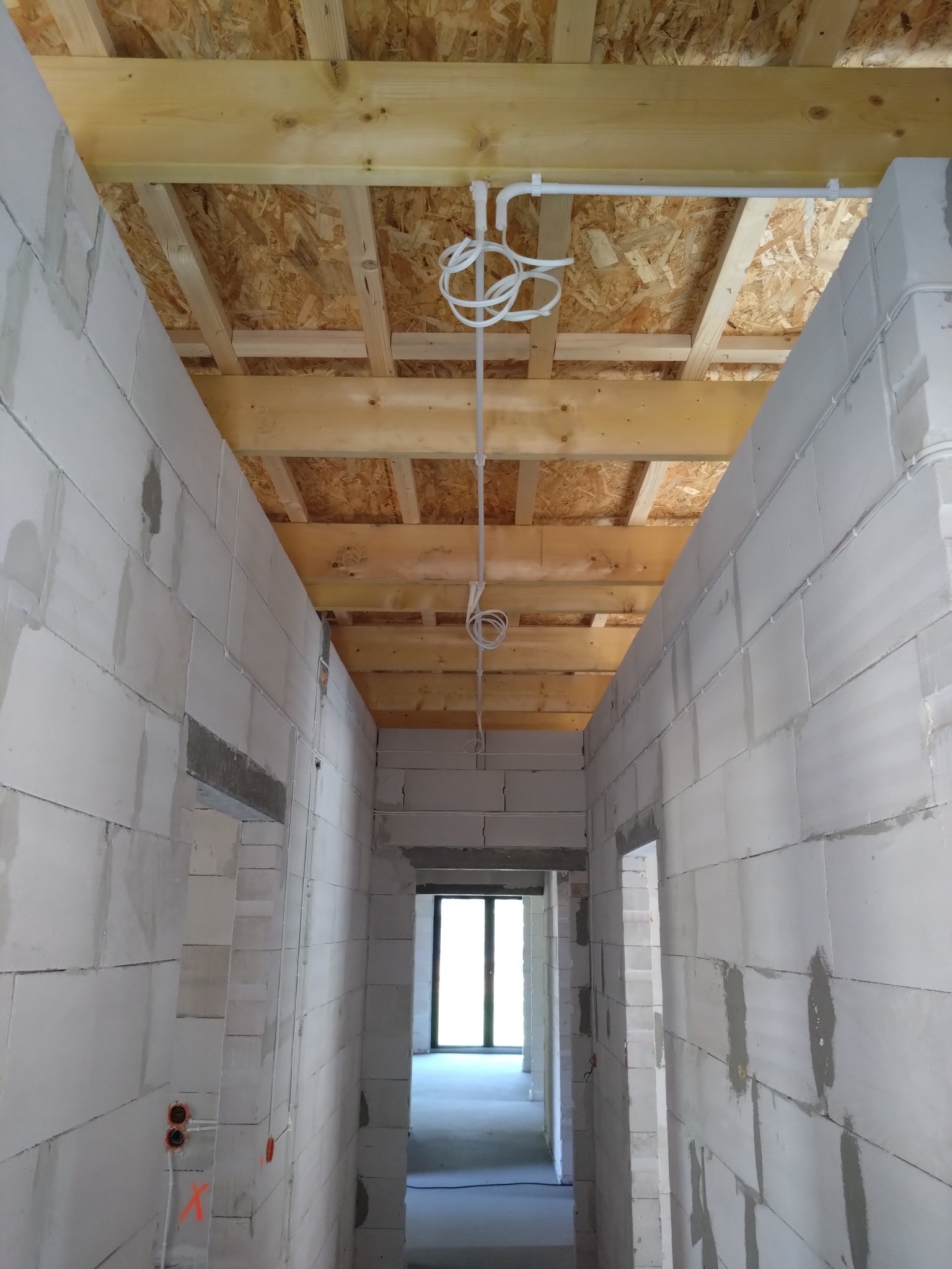 Wewnętrzne ściany z betonu komórkowego w surowym stanie z widoczną instalacją elektryczną w rurkach PCV pod stropem z desek i płyt OSB, przewody zwisają luźno.