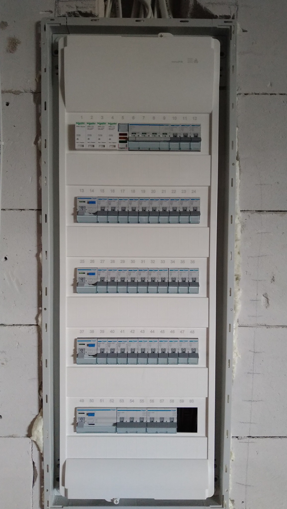 Rozdzielnica elektryczna z zamontowanymi bezpiecznikami, widok z bliska na ścianie z białych pustaków, częściowo wypełniona pianką montażową.