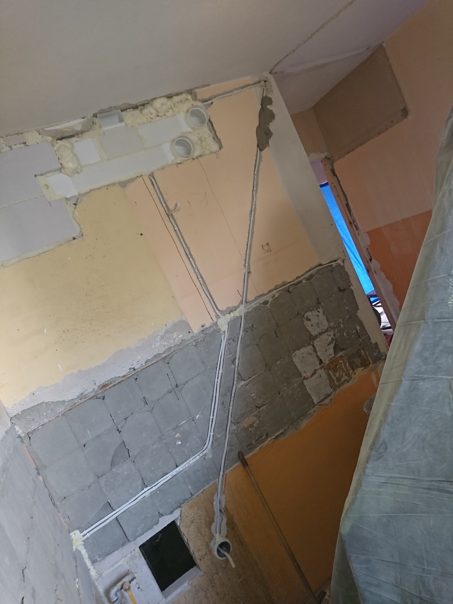 Wnętrze w trakcie remontu, widoczne kable elektryczne prowadzone po ścianach, częściowo zakryte pianką montażową i gładzią, z odsłoniętą instalacją podtynkową i fragmentami starej glazury na ścianie.