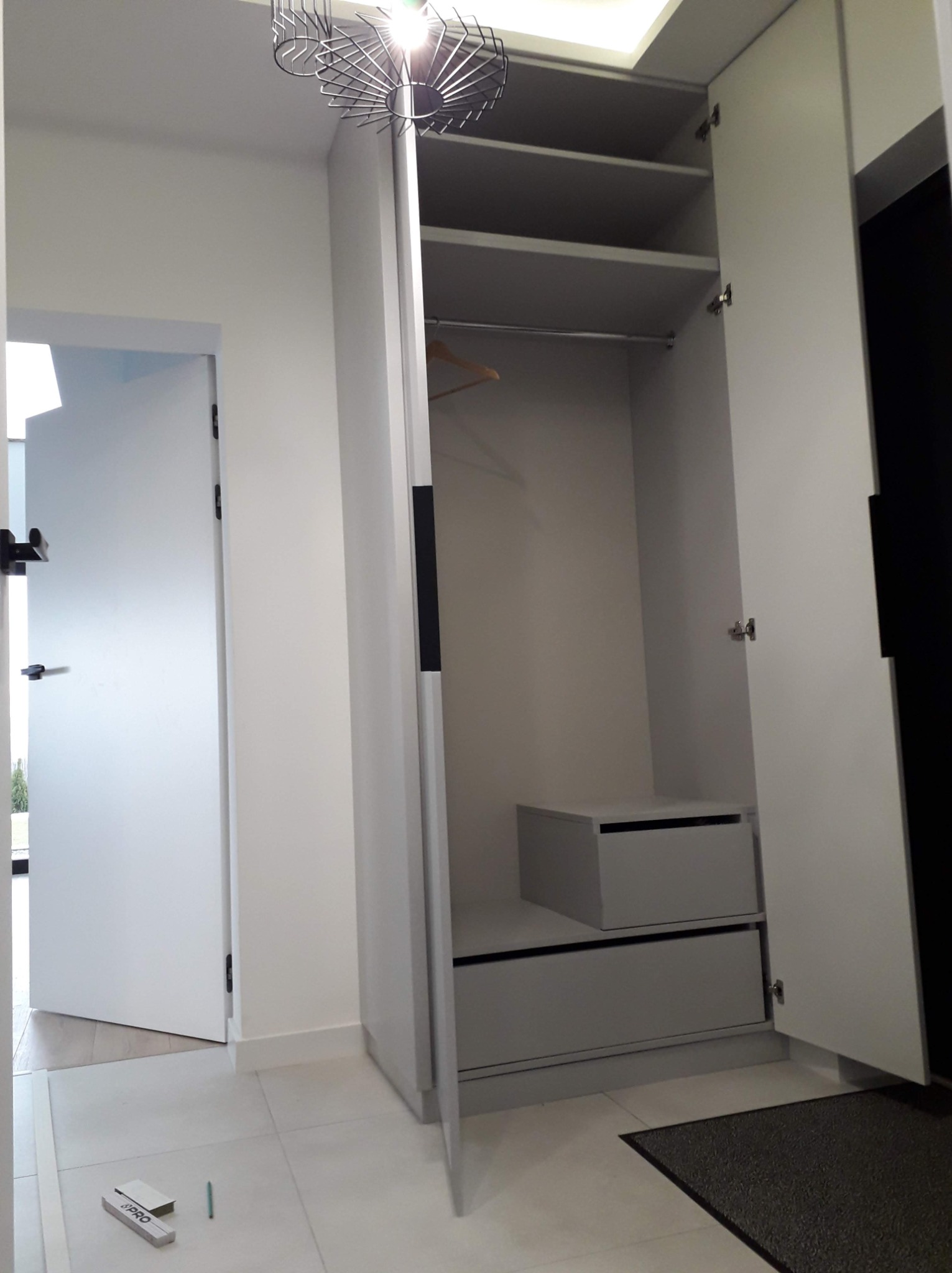 Wnętrze szafy wnękowej z półkami i szufladami, widoczne narzędzia pomiarowe na podłodze sugerujące montaż.