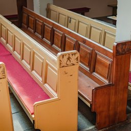 Skrzypek Laser Czyszczący - Rzędy drewnianych ławek kościelnych z czerwonymi siedziskami, widoczne detale snycerskie na oparciach, różne odcienie drewna