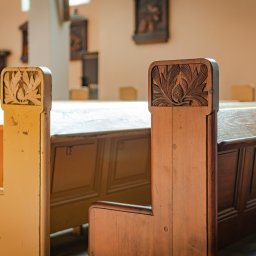 Skrzypek Laser Czyszczący - Drewniane ławki w kościele lub innym zabytkowym budynku, z dekoracyjnymi płaskorzeźbami szyszek i liści na oparciach, jedna ławka pomalowana na kremowo, druga w naturalnym kolorze drewna.