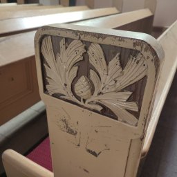 Skrzypek Laser Czyszczący - Detal zdobionego, odrapanego oparcia ławki kościelnej z motywem roślinnym i szyszki na tle rzędów ławek.