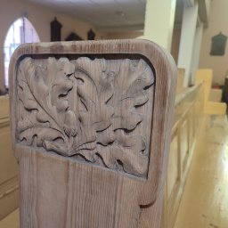 Skrzypek Laser Czyszczący - Drewniana ławka kościelna z płaskorzeźbą liści dębu i żołędzi na oparciu.