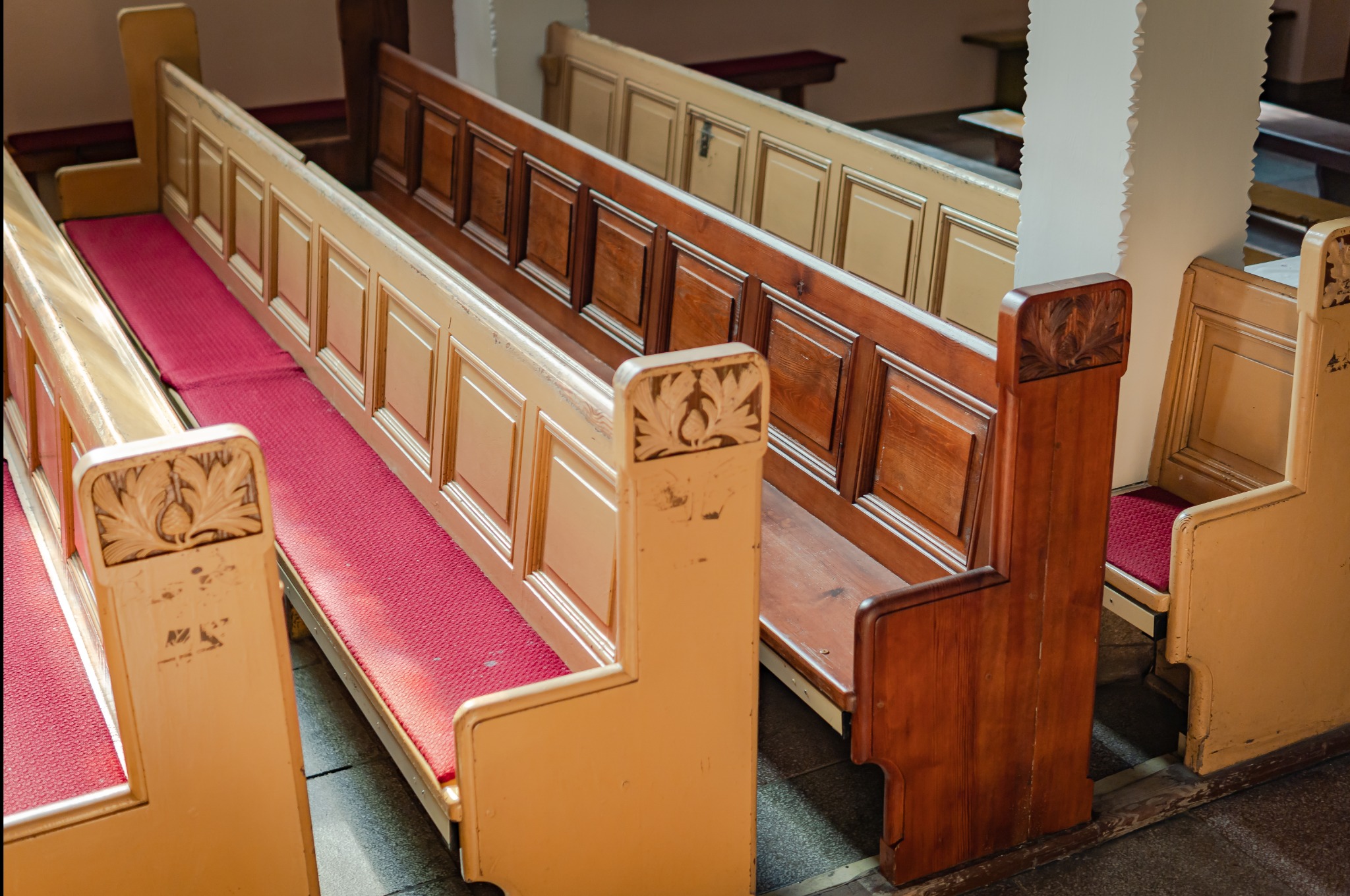 Rzędy drewnianych ławek kościelnych z czerwonymi siedziskami, widoczne detale snycerskie na oparciach, różne odcienie drewna