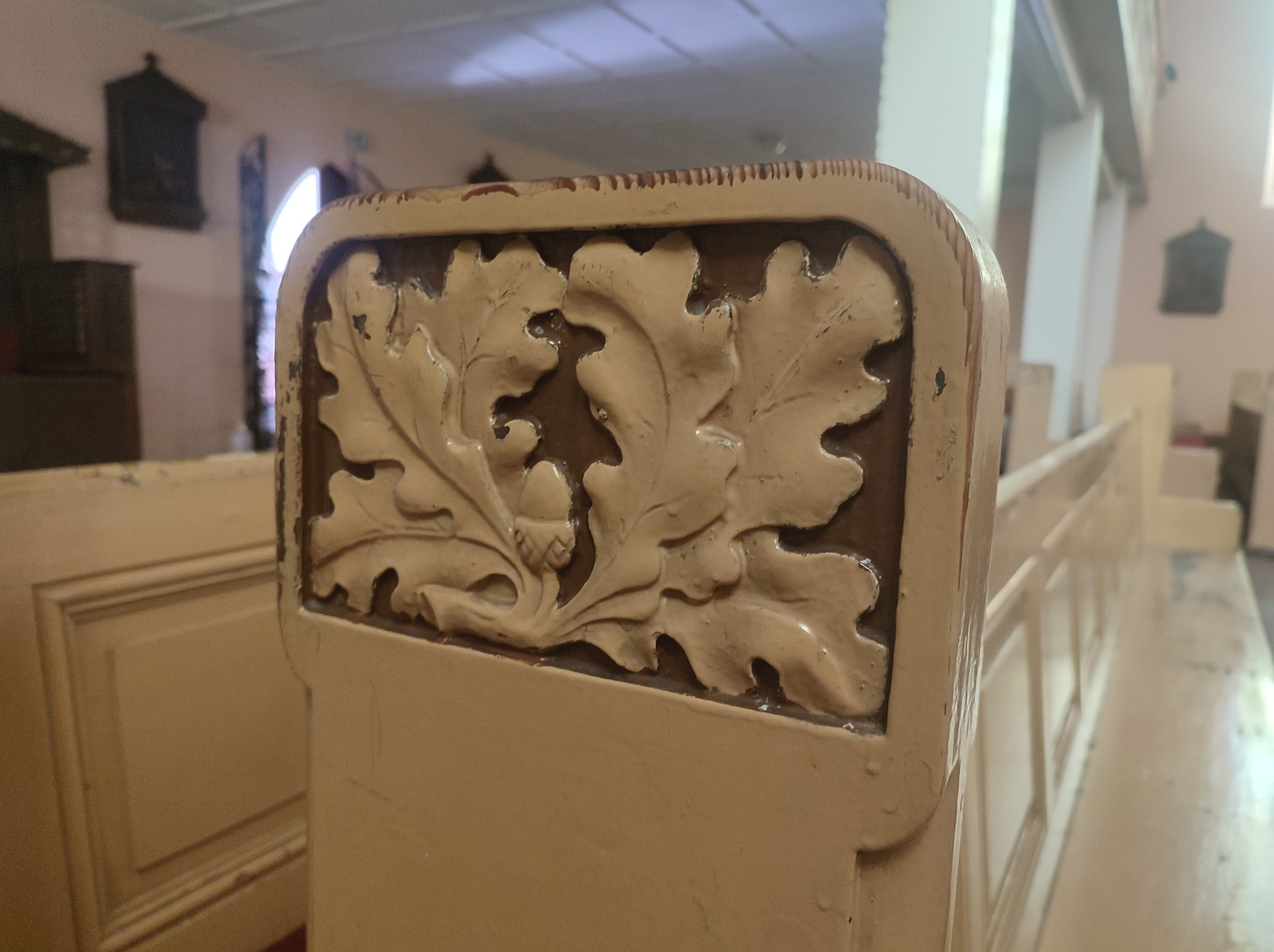 Detal zdobienia ławki kościelnej z motywem liści dębu i żołędzi, widoczne ślady użytkowania i odnowień.