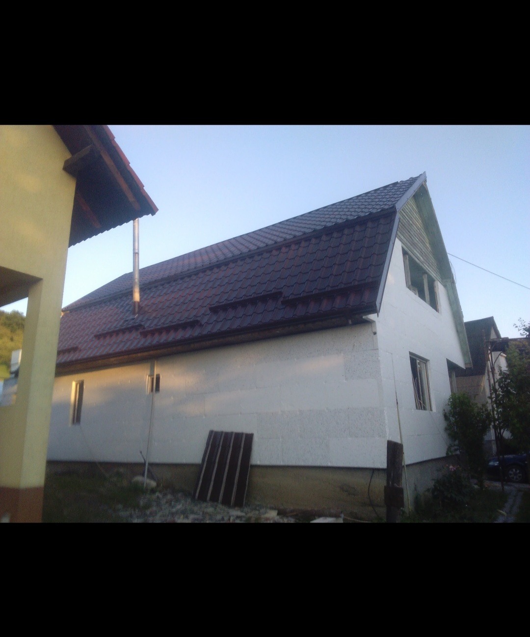 Dom jednorodzinny z nowym, ciemnym dachem z blachodachówki, w trakcie ocieplania ścian zewnętrznych styropianem, widoczne rynny i komin.