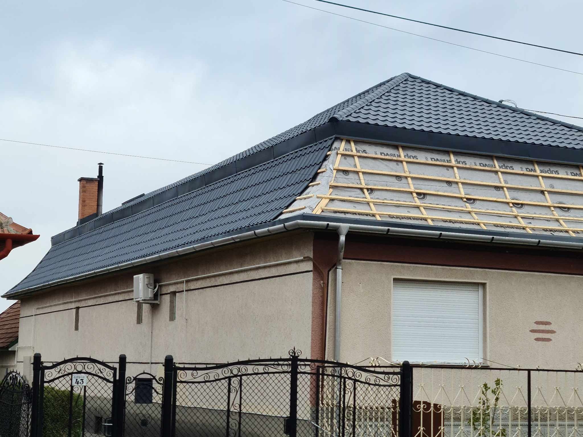 Dom jednorodzinny z częściowo położonym, ciemnoszarym dachem z blachy trapezowej i widoczną konstrukcją drewnianą pod spodem, zabezpieczoną membraną dachową.