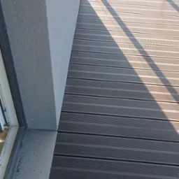 Szare deski tarasowe ułożone na balkonie, widok z góry, cień rzucany przez barierkę, widok na plac z budynkami w tle.