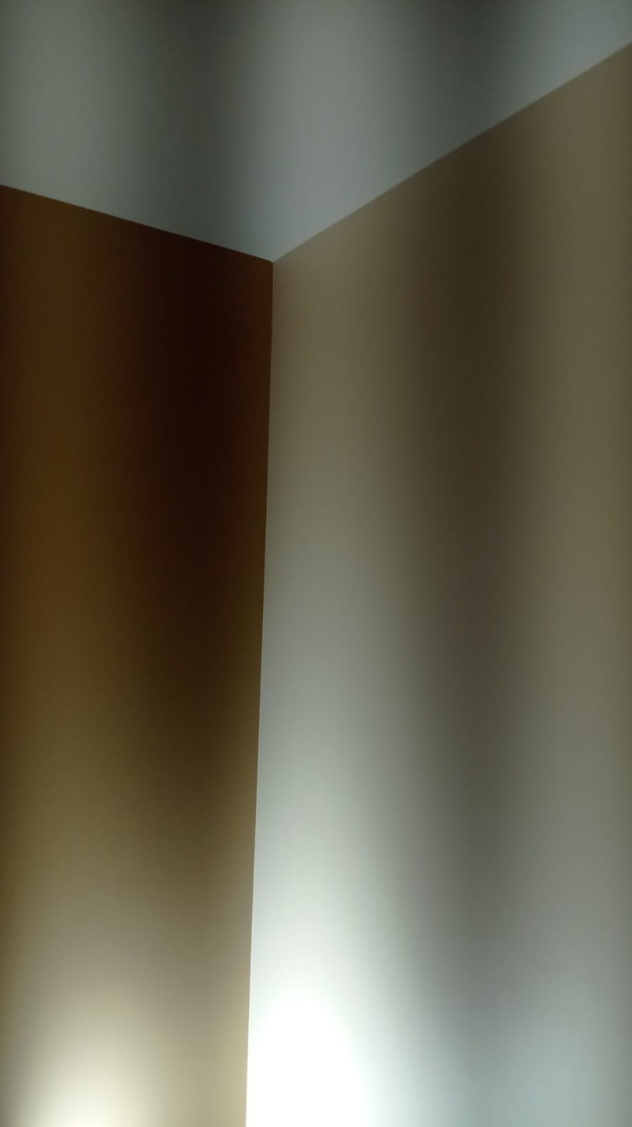 Pomieszczenie z pomalowanymi ścianami na kolor brązowy i beżowy, widoczne łączenie ścian i sufitu.