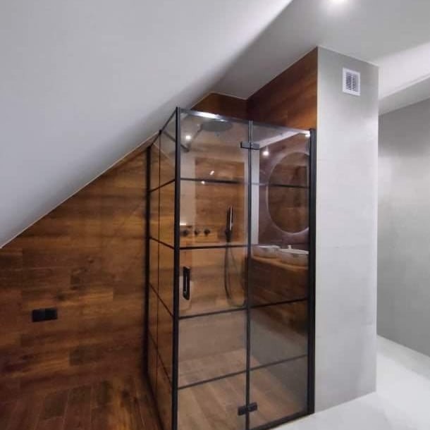 Kabina prysznicowa w stylu loft z czarnymi szprosami na tle drewnianej ściany i skośnego sufitu w wykończonej łazience.